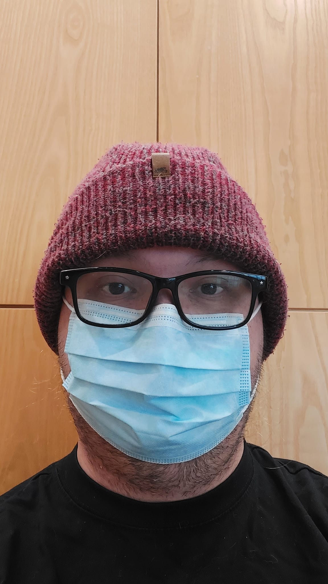 A man wears a red toque and surgical mask sits inside a hospital waiting room